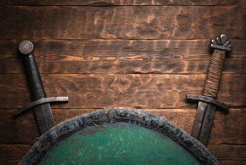 Two swords and the shield on the old medieval table flat lay concept background with copy space.