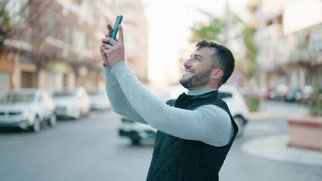 Young hispanic man smiling confident making picture by the smartphone at street