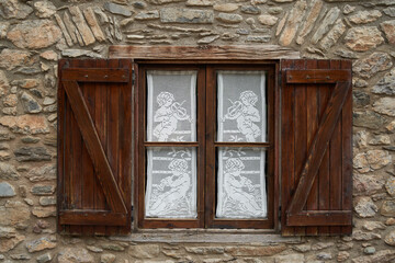 Antique wooden window with white curtains containing drawings musicians on an old stone house. Rustic architecture and countryside concept.