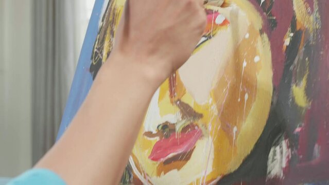 Close Up Of A Hand Holding Paintbrush And Mixing It With Colour Before Painting A Girl'S Face On The Canvas
