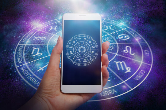 female hand holding smartphone device with astrology app over cosmic space background. Zodiac circle concept.