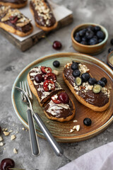 Eclairs with chocolate topping, nuts and berries. Chocolate, nut, banana, cherry and blueberry eclairs. Dessert on a plate. Top view