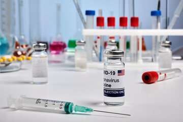 American Covid vaccine and syringe in a lab. Science photo for pharmacy exploration laboratory. Antivirus vaccine for coronavirus therapy. Photo for pharmacy drugstores. Chemical glassware on desk.