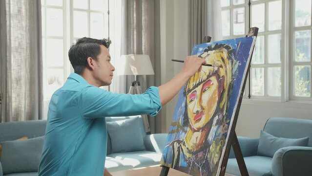 Medium Shot Side View Of An Asian Artist Man Holding Paintbrush Mixed Colour And Thinking Before Painting A Girl'S Hair On The Canvas

