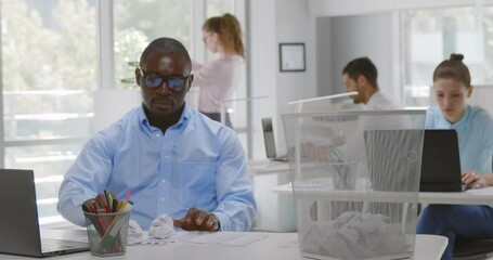 Afro-american businessman throw crumpled ball of paper into trash can in office - Powered by Adobe