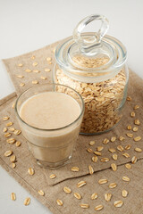 Oat milk in a glass and jar with oatmeal on a white and gray background. Milk substitute, milk for vegetarians. Copy space.
