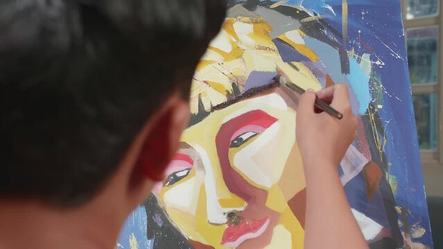 Close Up Of An Asian Artist Boy Holding Paintbrush Mixed Colour And Painting A Girl'S Face On The Canvas

