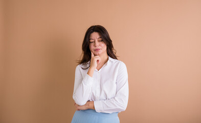 a frustrated brunette woman in a white shirt stands on a beige background with a place for text