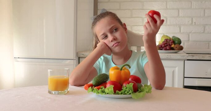 Unhappy child sitting at breakfast. Portrait of a child with vegetables in the kitchen. the child does not want to eat vegetables and fruits