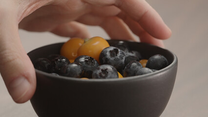 man hand take blueberries and physalis from black bowl