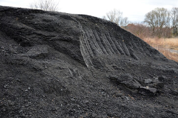 recycled asphalt from road milling on a large pile at a landfill. traces of a grab from an...
