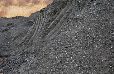 recycled asphalt from road milling on a large pile at a landfill. traces of a grab from an...