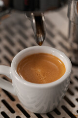 White cup with espresso on coffee machine tray