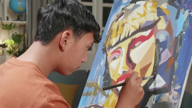 Close Up Side View Of An Asian Artist Boy Holding Paintbrush Mixed Colour And Painting A Girl'S Face On The Canvas
