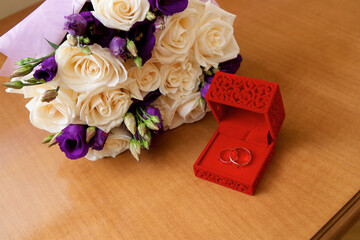 Wedding rings are in a box on the table next to the wedding bouquet.