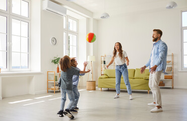 Happy family playing ball in the house. Cheerful young mother, father and little children playing...
