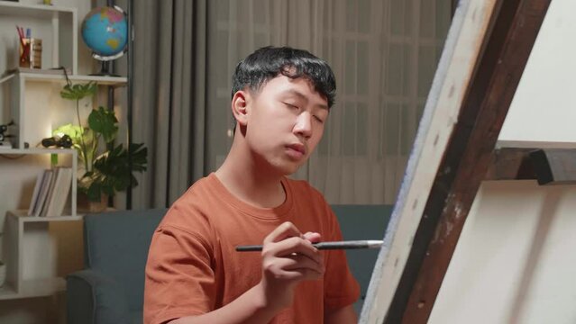 Medium Close Up Of An Asian Artist Boy Holding Paintbrush Mixed Colour And Thinking Before Painting On The Canvas
