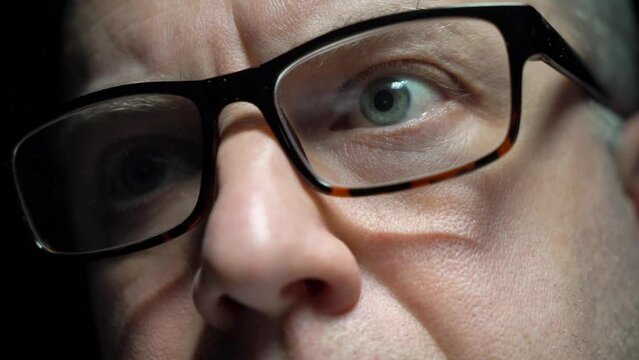 Close-up of focused middle age man wearing computer glasses for reducing eye strain, browsing internet, reading news, watching screen working online late. Tracking dolli shot