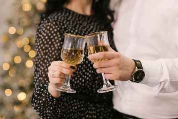 Women's and men's hands with glasses of sparkling wine on the background of the Christmas tree