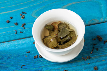 green tea is brewed in a white bowl on a blue wooden background. Dry tea leaves lie nearby. Top view