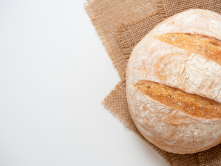 A close-up of freshly baked wheat bread with a crispy crust lies on a linen cloth on a white background. Top view flat lay, copy space