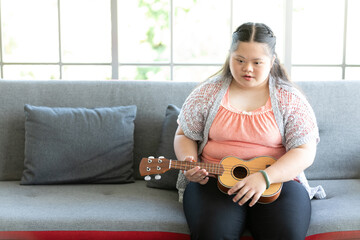 a girl with down syndrome singing and playing ukulele or small guitar on sofa