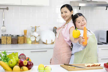 down syndrome teenage girl and her mother showing carrot and yellow pepper in the kitchen