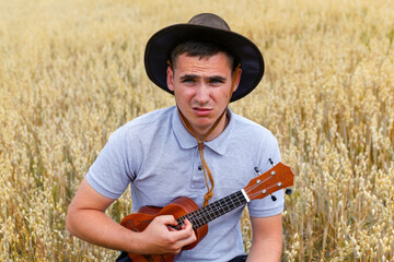 Sad person. Young beautiful caucasian man playing ukulele outside. Handsome hipster guy plays...