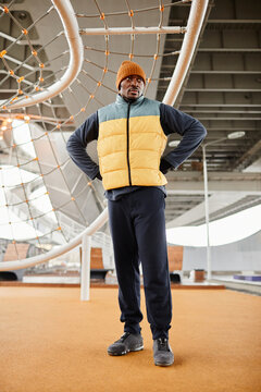 Young serious African American athlete standing on sports ground with facilities against rope net for pulling up and crowling