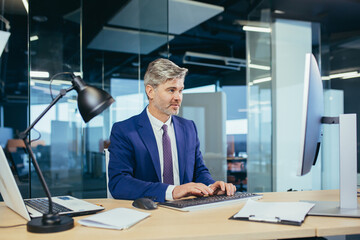 Pensive boss working at computer in modern office, successful male businessman