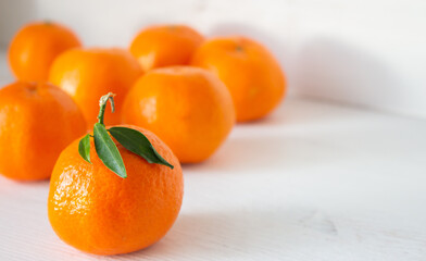 Sweet citrus fruits. Ripe mandarins clementine on white wooden background. One against all concept. Stay different concept. One mandarin with leaf and group of fruits without leaves. Vitamin C concept