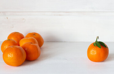 Sweet citrus fruits. Ripe mandarins clementine on white wooden background. One against all concept....