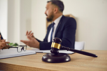 Close up of judge's gavel on wooden table, with lawyer giving consultation in background,...