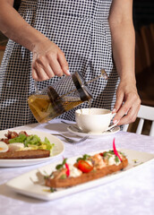 Woman pours green tea for breakfast. On the table are sandwiches, bread, egg, bacon