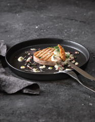 grilled tuna steak with sauce, black round plate on dark background