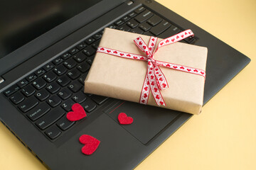 gift box tied with ribbon, red hearts, laptop on yellow background. valentine's day concept