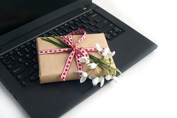 a bouquet of snowdrops, a gift box tied with a ribbon, on a laptop on a white background close-up. congratulations on March 8, mother's day, birthday. romantic background.