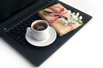 a cup of coffee, a bouquet of snowdrops, a gift box tied with a ribbon, on a laptop on a white background. congratulations on March 8, mother's day, birthday. romantic background.