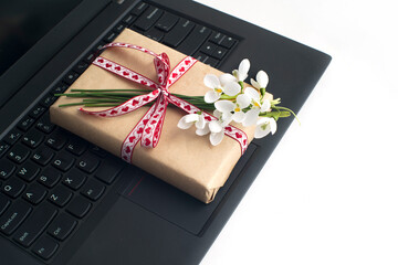 a bouquet of snowdrops, a gift box tied with a ribbon, on a laptop on a white background close-up. congratulations on March 8, mother's day, birthday. romantic background.
