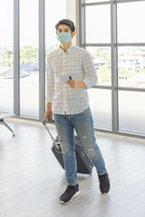 A young Asian passenger with his passport and boarding pass wait in an airport terminal for his flight with masks on and keep social distance