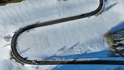 Luftaufnahme mit einer Drohne von einer verschneiten Landschaft mit einer kurvigen Straße mit Autos