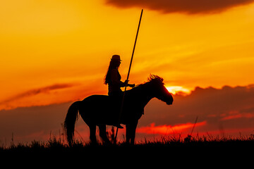 beautiful woman with long hair like a silhouette with a long spear at sunset
