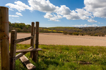A footpath stile on the South Downs Way, near East Marden Down, with arable fields beyond, and a blue sky with white cumulus clouds: South Downs National Park, West Sussex, UK