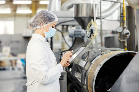 A food factory inspector scrolling on tablet while standing next to a boiler.