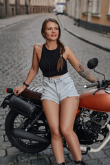 Tattooed female motorcyclist posing with retro bike outdoors