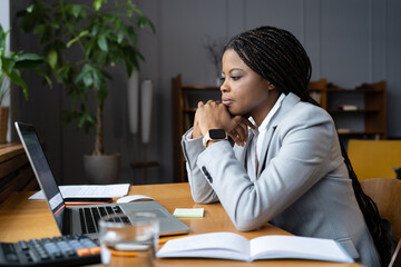 Serious african american businesswoman sitting at table looking at laptop screen. Ethnic woman read...
