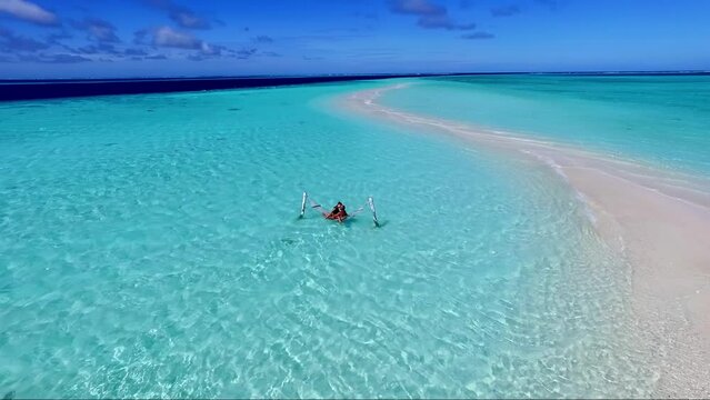 A young woman and a man in a hammock enjoy a tropical vacation in the Maldives. People travel leisure. A girl and a guy are resting in a hammock over the sea, looking at the seascape.
