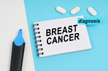 On a white and blue surface are pills, a marker and a notebook with the inscription - BREAST CANCER