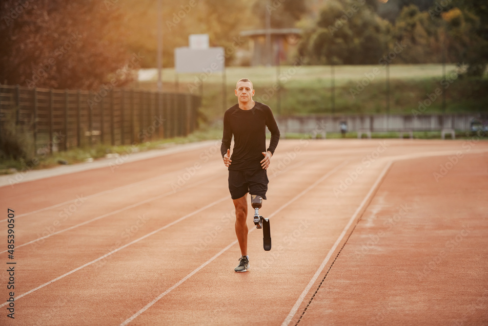 Poster a healthy handicapped runner with artificial leg running on running track at stadium.