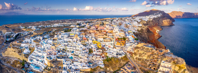 Fototapeta premium Picturesque Aerial drone view of famous Oia village with white houses during sunrise on Santorini island, Greece, Europe. Luxury travel. Summer holidays. Travel concept background.